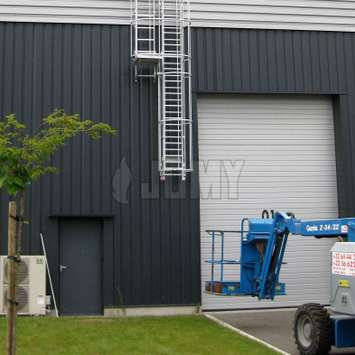 Drop-down ladder - Warehouse - Double cage and resting platform Drop-down ladder with double cage and resting platform outside of a warehouse.